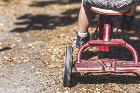 Photographie d'un enfant sur un tricycle. La photographie est cadrée sur le tricycle.