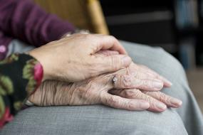 Photographie en gros plan sur la main qui repose sur les mains d'une personne âgée.