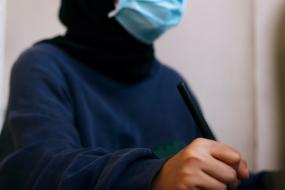 Photographie d'une personne portant un masque est tenant un crayon en position d'écriture.