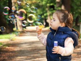Photographie d'un enfant sur un sentier dans les bois qui souffle des bulles de savon.