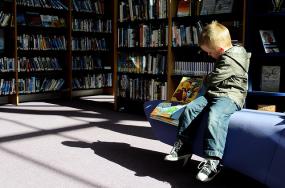 Un enfant lit un livre sur un fauteuil dans bibliothèque.
