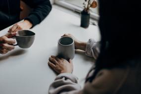 Deux personnes face à face discutent avec un café à la main.