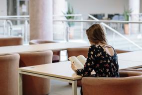 Photographie d'une femme légèrement de dos qui lit assise à une table.